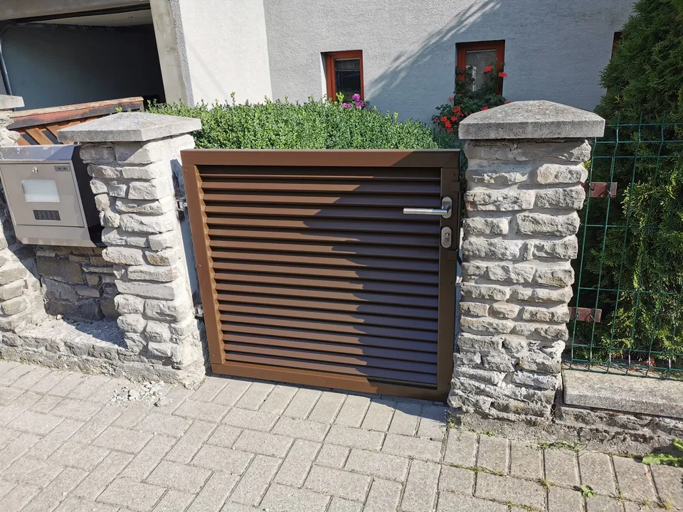 Hnedá žalúziová bránka medzi kamennými stĺpmi
